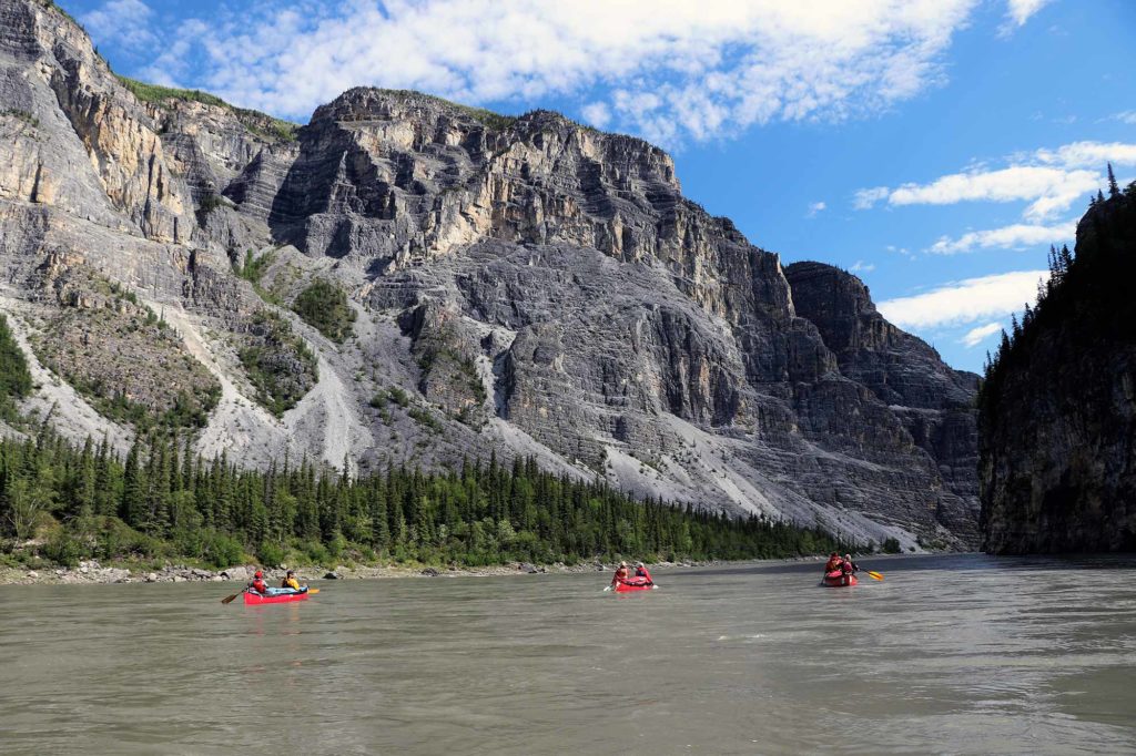 people kayaking in a river with Nahanni National Park Reserve in the background