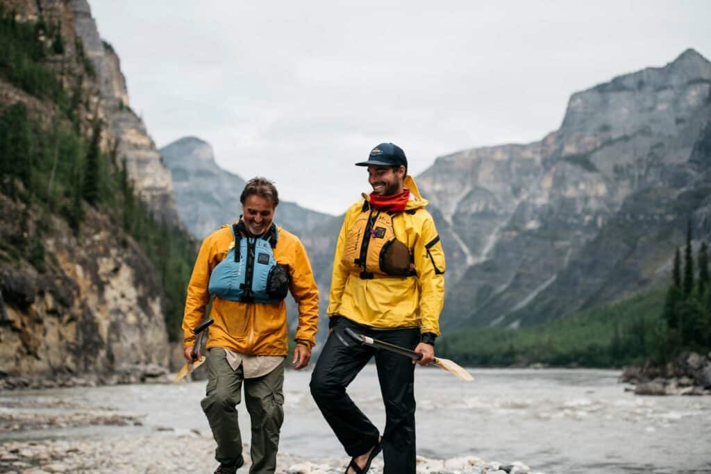 two men in yellow jackets walking on a rocky shore
