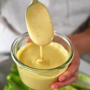 A spoon dipping into a jar of dairy-free Caesar Dressing.