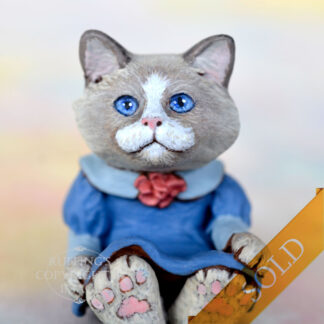 A bi-color ragdoll kitten in a blue dress with a light blue collar and a mauve rose in the middle of her neckline marked sold