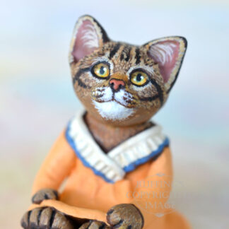 tabby kitten figurine in a light orange dress with a cream colored ruffle at the neck with blue trim