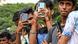 Several young men stand outdoors holding smartphones, taking photos or videos. The focus is on their hands and devices, with a blurred green background Several young men stand outdoors holding smartphones, taking photos or videos. The focus is on their hands and devices, with a blurred green background