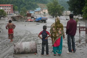 People stand, looking out at a flooded road.
