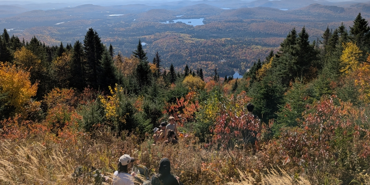 00Feature image_MEC Laval story_credit Marc-André Aubin | Trans Canada Trail two people sitting at hike lookout over fall foliage and lakes below