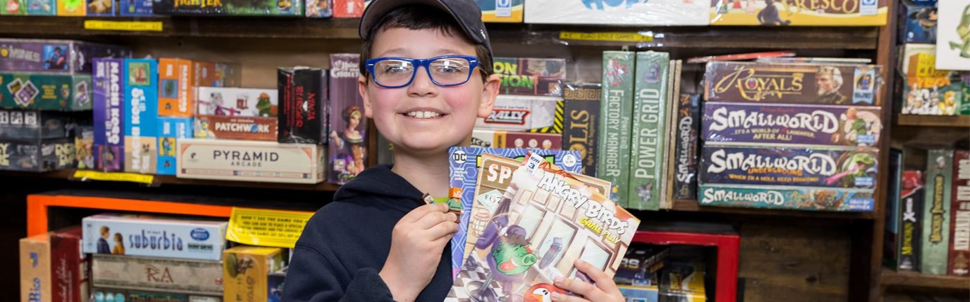 Boy in front of board games, holding free comics! Boy holding comic books