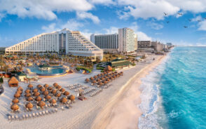 Featured image for a guide titled Is Cancun Safe to Visit featuring a bunch of resorts lining the teal water on the coast