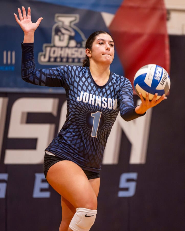 A young woman holding a volleyball in one hand as she prepares to serve it during a game