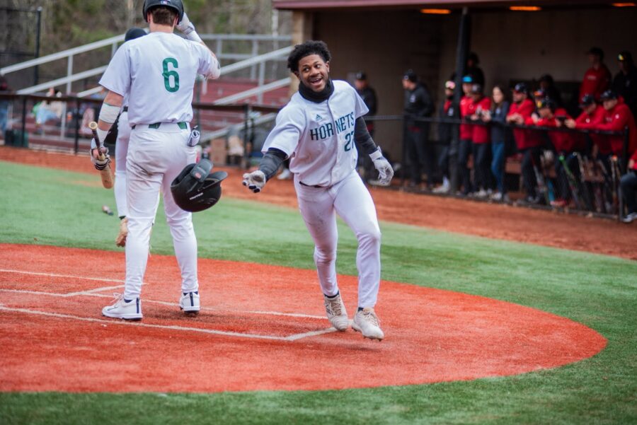 A VTSU Lyndon baseball player rounding a base and grinning with his arm outstretched