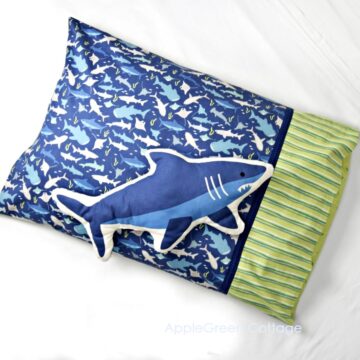a beautiful handmade pillowcase in blue sea fish prints and a green striped quilting cotton, next to a sewn fabric shark toy in the same colors