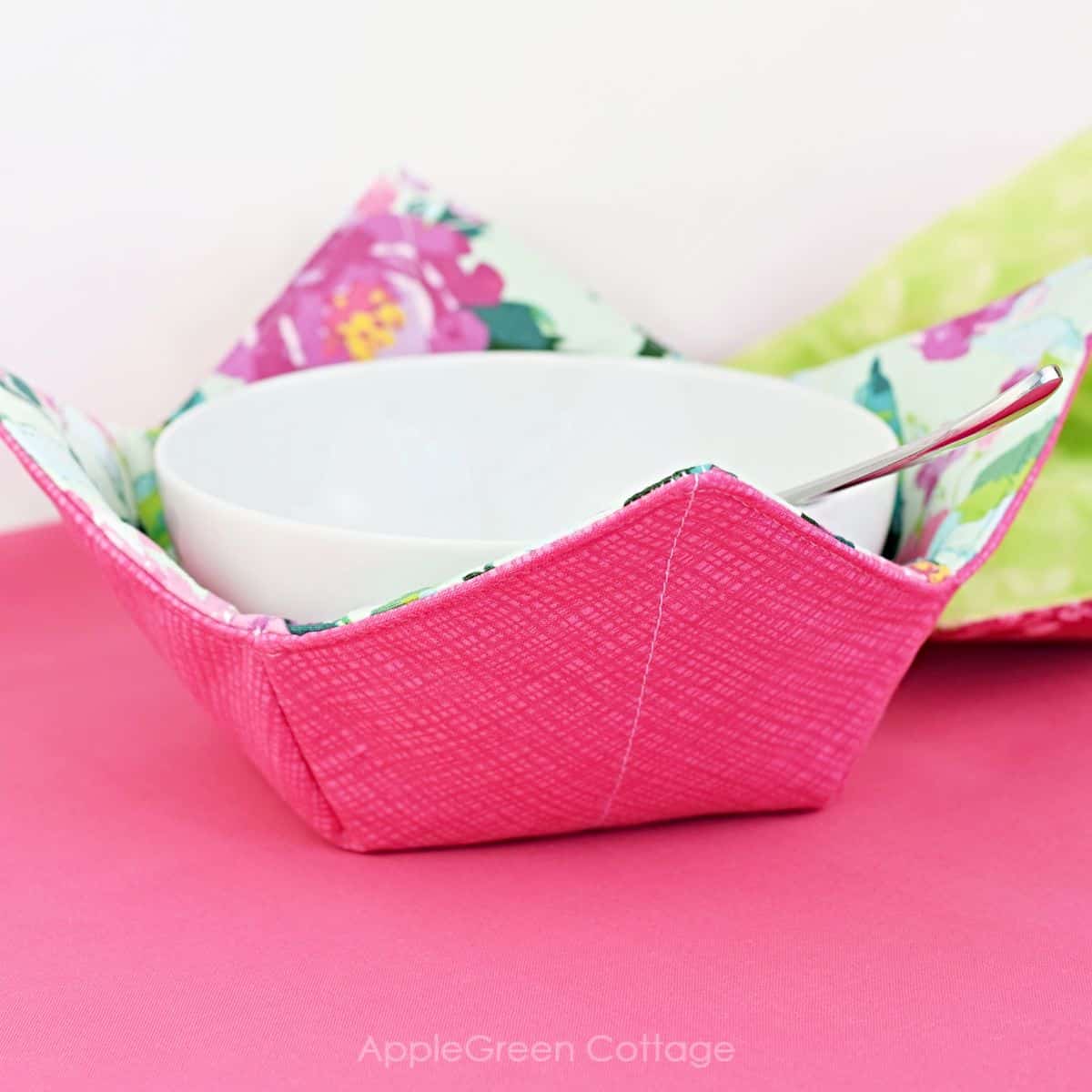 a floral fabric bowl cozy placed on a pink tablecloth