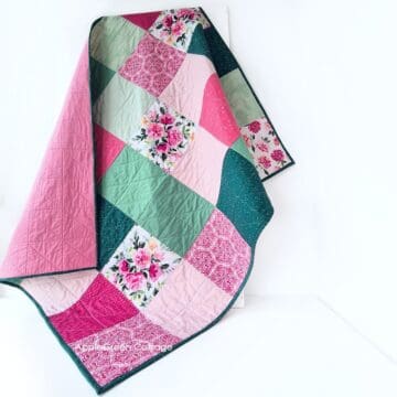 Handmade patchwork quilt in pink and green with floral pattern squares, featuring quilted stitching and dark green binding.