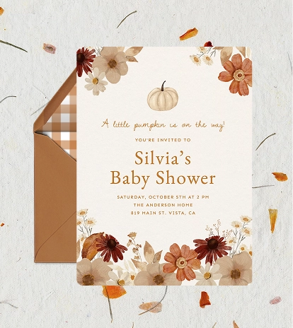 A baby shower invitation on a beige background with watercolor autumnal leaves, flowers, and one white pumpkin in the center.