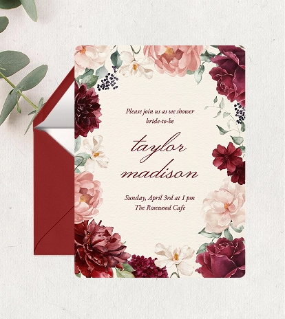 A bridal shower invitation on a blush pink background surrounded by a frame of pink, burgundy, and white flowers.