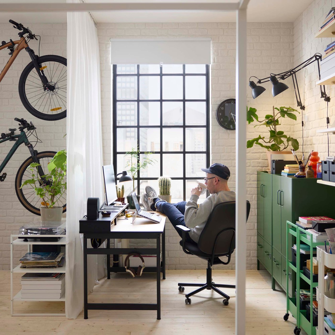 A person sits with their foot up on their desk in an industrial loft-style apartment in front of a window.