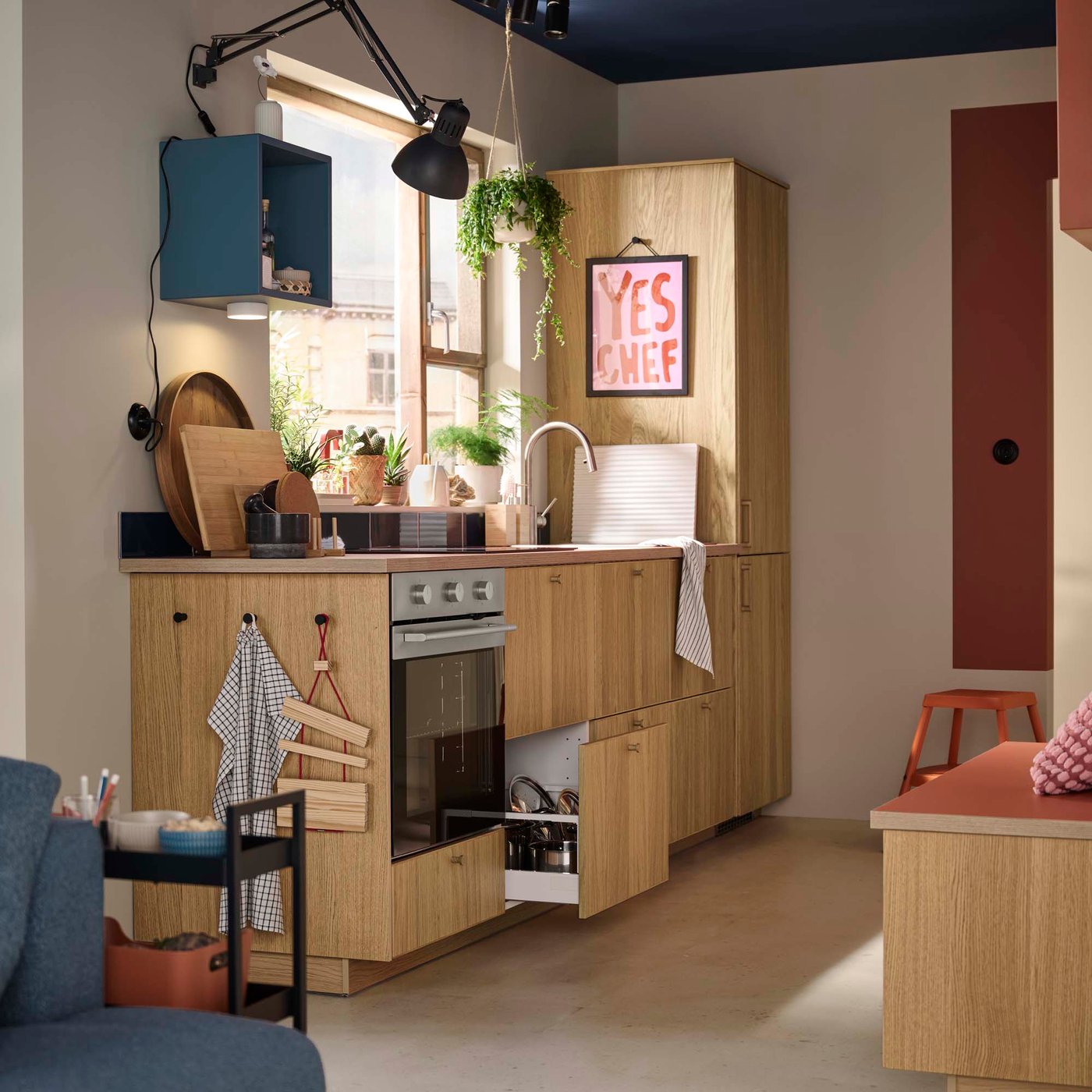 A kitchen with light oak veneer cabinets and blue and red accents.