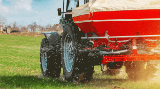A red farm vehicle spreads NPK fertilizer, which contains nitrogen, phosphorus, and potassium.