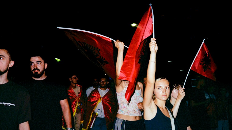 Crowd of protesters at night holding red Albanian flags.