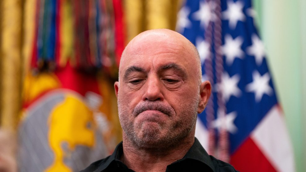 Joe Rogan frowns and looks downwards while standing in the Oval Office