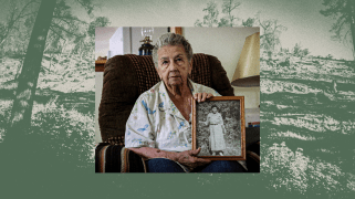 A collage of two photographs. In the foreground, an elderly woman in a plush brown lounger sits up as she holds a framed black-and-white photo of her grandmother. In the background, a photo in green-and-black tint reveals a barren hillside with sparse trees.