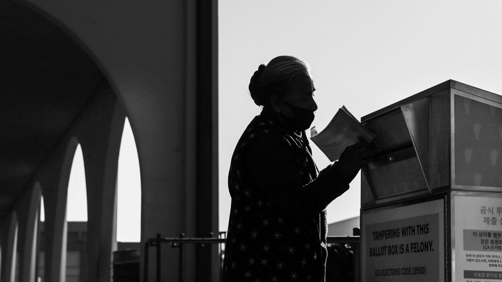 Black and white photo of a person dropping a ballot into a ballot drop box.