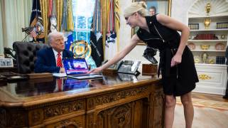 Donald Trump in the Oval Office, with Natalie Harp leaning over to hand him something