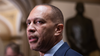 A headshot of Hakeem Jeffries inside a building. He is looking to his left and is wearing a suit.