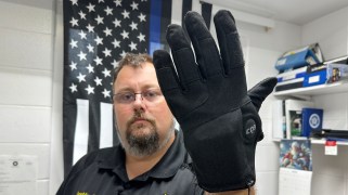 A man holds up a shock glove in front of a blue lives matter flag.