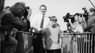 A black-and-white photo of Tony Blair campaigning with his son, Nick Blair, who is in this instance a child. It is 1997.