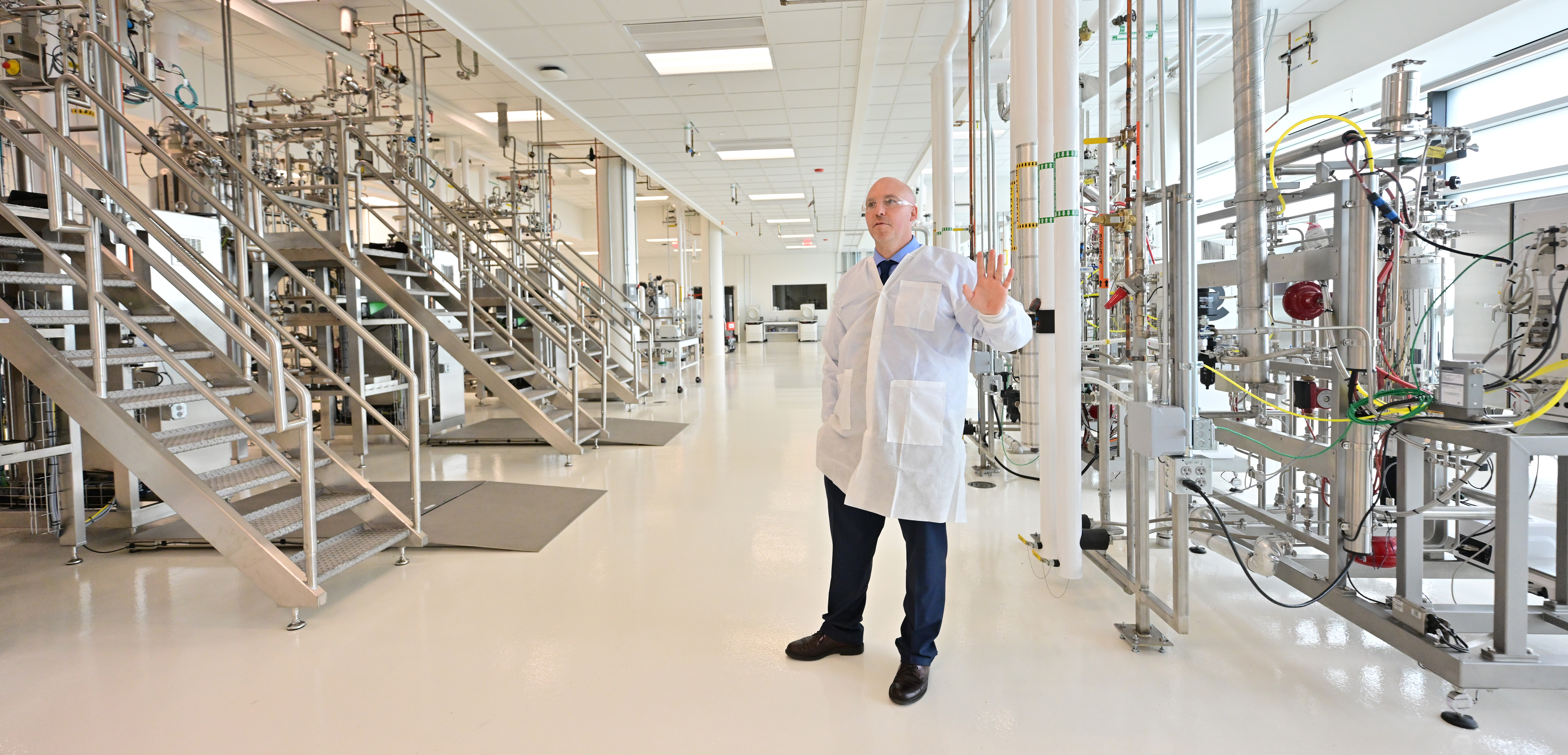 STP-L-BIO-0819 Marcus Schicklberger, wearing a white lab coat, gestures while talking in a biomanufacturing facility.