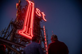 STP-L-FIRSTSIGN-01 Two people look up at a towering, glowing red '1st' sign